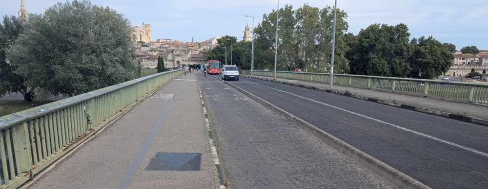 Hochbord-Gehweg, der bis vor wenigen Jahren je zur Hälfte ein sehr schmaler Gehweg und ein sehr schmaler Radweg war, daneben der neue 2-Richtungs-Radweg, dann eine schmale Betonkante von ca. 10 cm Höhe und Breite. Die verbleibende Fahrbahn reicht gerade noch für den Begegnungsverkehr von 2 Bussen.