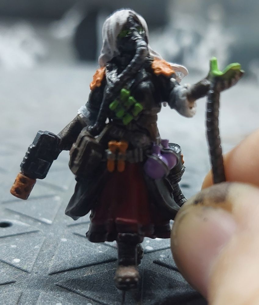 Woman with white hair and black coat offering mechanics contraptions and vials. 