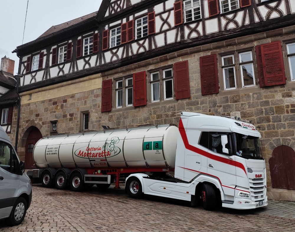 Ein weißer Tank-LKW, der vor der Sektkellerei Kessler, einem alten Fachwerkhaus, steht und vermutlich Wein liefert. Auf dem LKW steht "Latteria Mortaretta", d.h. wurde der Tanklaster früher wohl für Milch eingesetzt.
