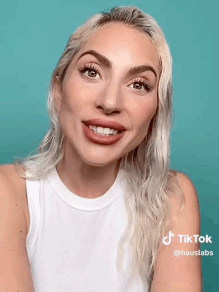 a woman with blonde hair and a white tank top is smiling .