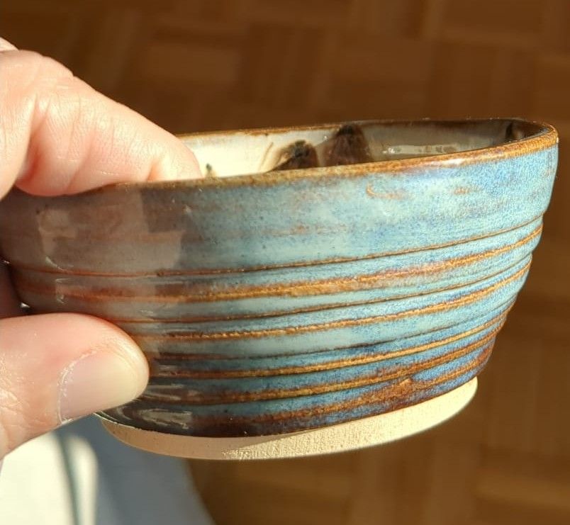 small bowl about the size of a fist, with a sea blue and brown shiny glaze. The bowl has carved horizontal ridges. The interior is brown and white.