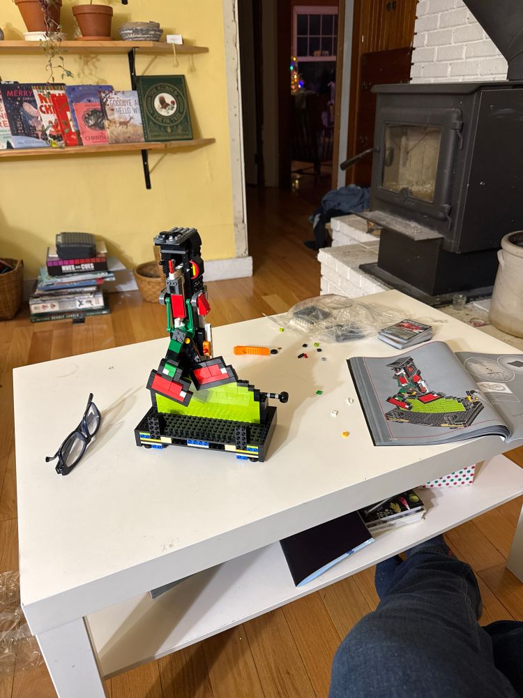 Partially done lego of Yoshi’s feet next to the instruction booklet on a white table. 