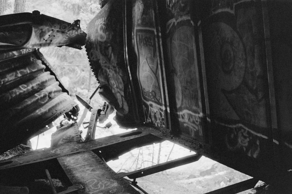 Graffiti covered mangled train car sitting over a river. The light outside is shining in and softening the sharp edges of the car. Ilford HP5+ at 1600 ISO, XT-3 1+1