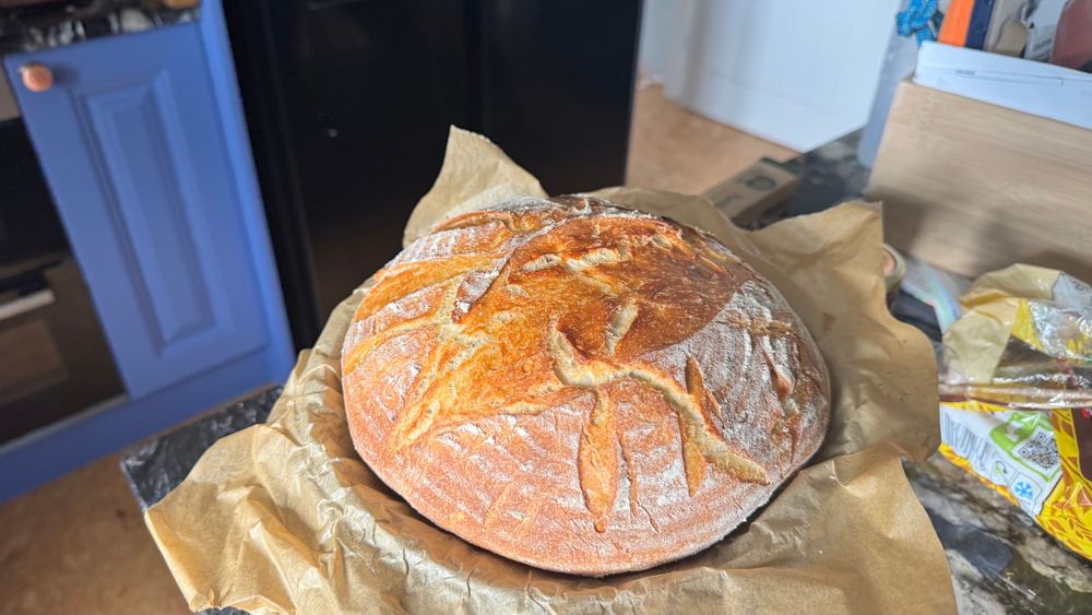 Another shot of the round cob loaf of sourdough, on a black marble counter top, with blue cabinet doors in the background.