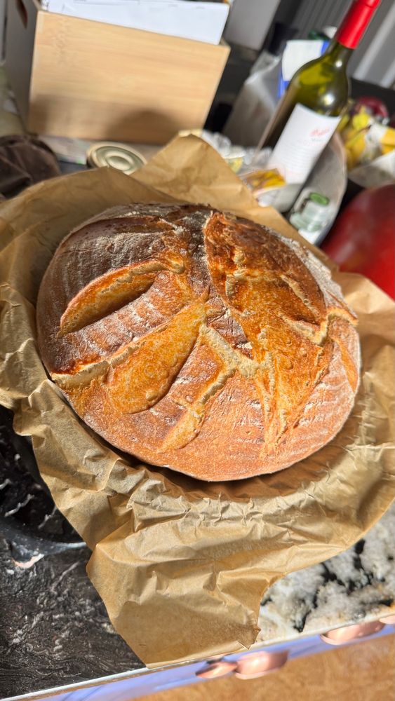A lovely golden brown, round cob loaf of sourdough, on a black marble counter top.