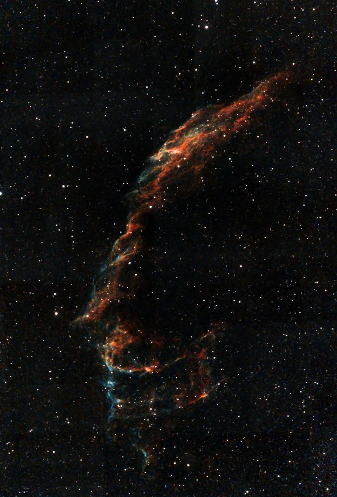 A colourful photograph of the Eastern Veil Nebula, which is a Supernova remnant located in the constellation Cygnus.  The colours of the various gases that make up the nebula are blue, red, yellow and orange.  