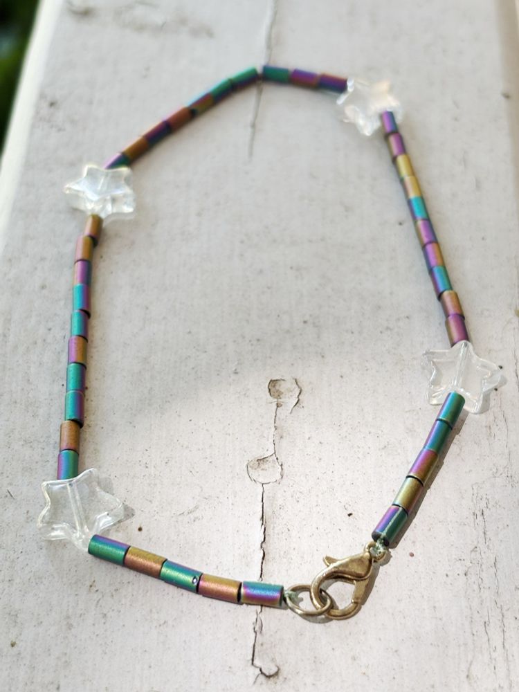 An anklet made with rainbow bugle beads and glass stars on a painted surface 