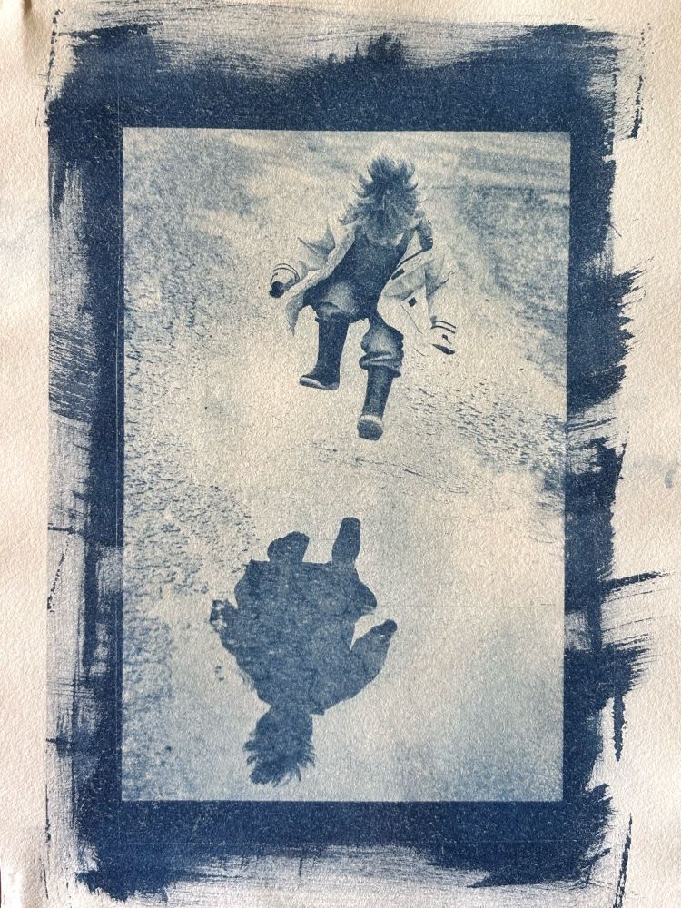A blue and white cyanotype print of a little boy mid-leap jumping into a puddle. 
