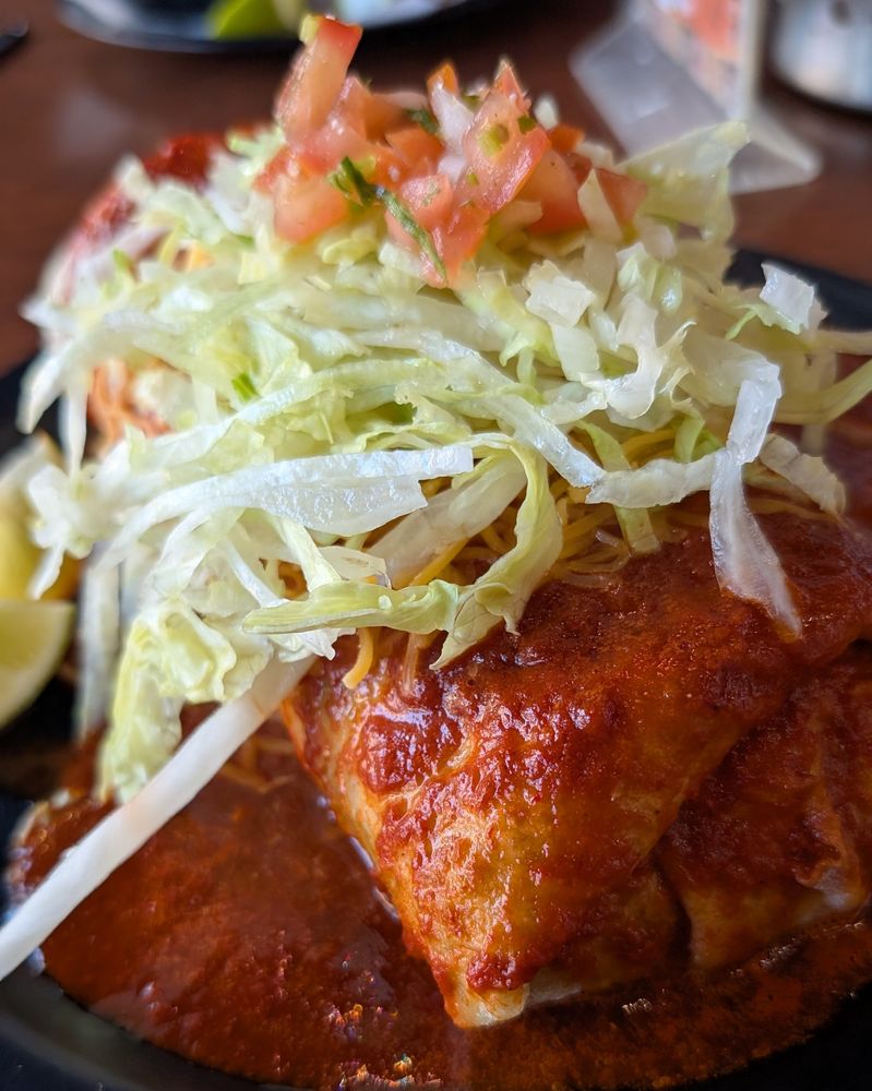 A beautiful burrito presented "wet style" covered in a spicy red sauce topped with iceberg lettuce and chopped tomatoes. On the side, some limes for some extra zestiness. Your taste buds can deflect flavor of this magnitude.