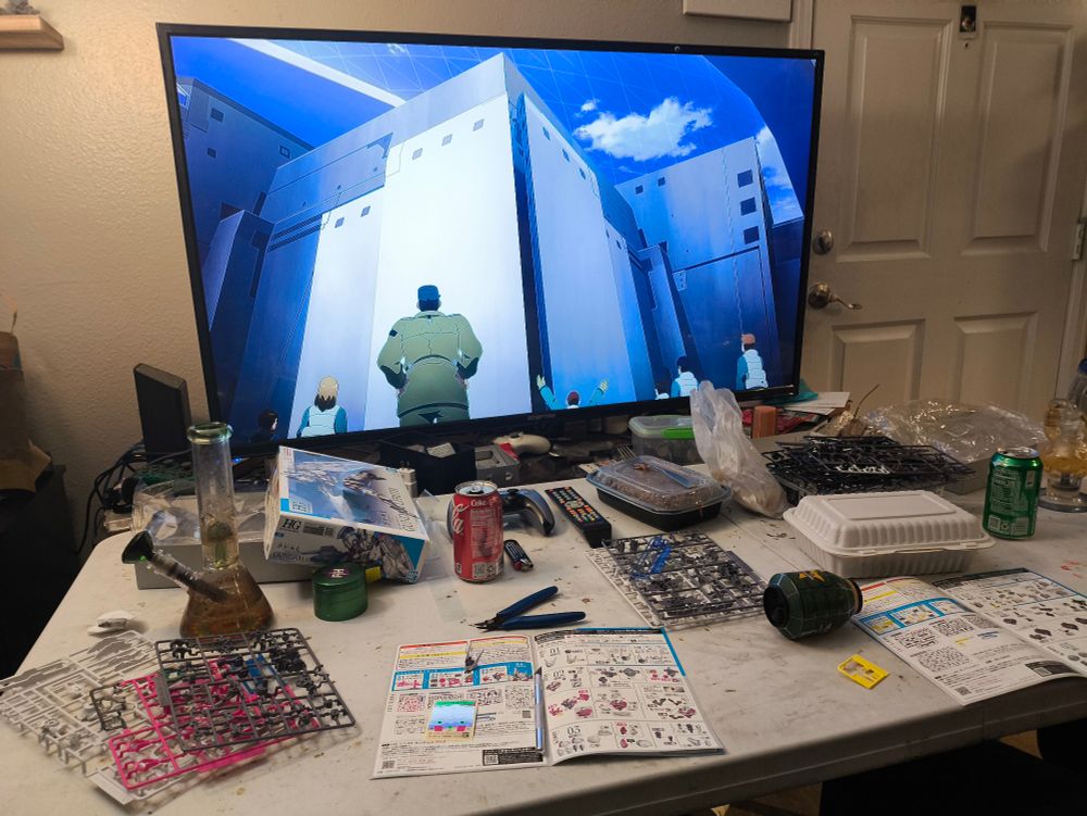 two gunpla kits in progress all over a table, there's also weed and Chinese food. Gundam Witch is on the tv