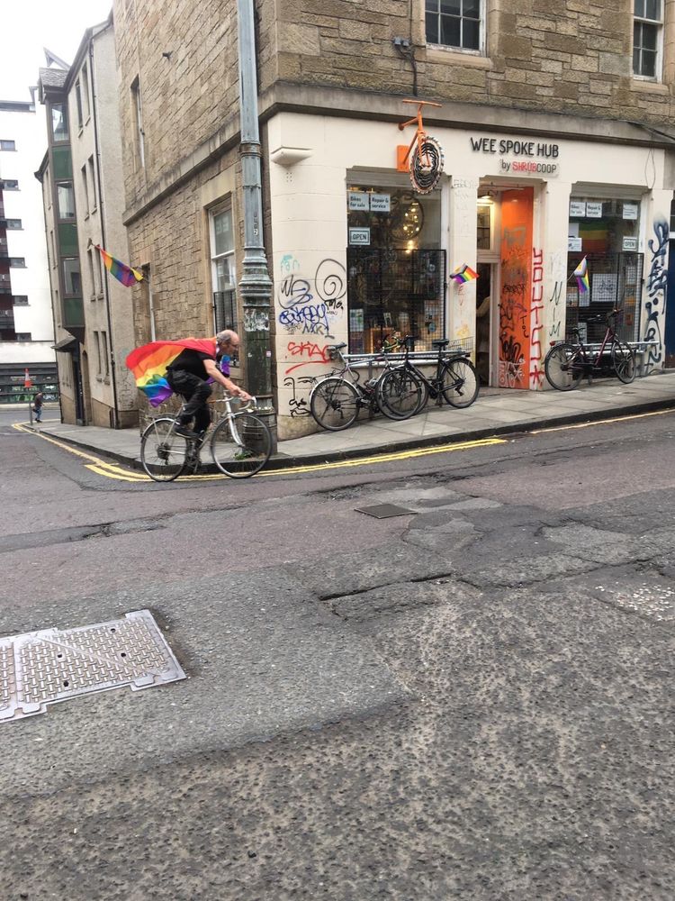 The same cycle mechanic with the Pride flag is cycling uphill around the lower corner in Guthrie Street, his Superman Pride cape aflutter.