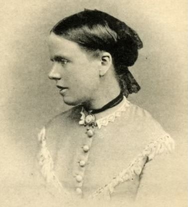 Sepia photograph of Julia Wedgwood. A young white woman with dark hair sitting in profile wearing a buttoned dress with lace collage and a ribbon choker with cameo pendant
