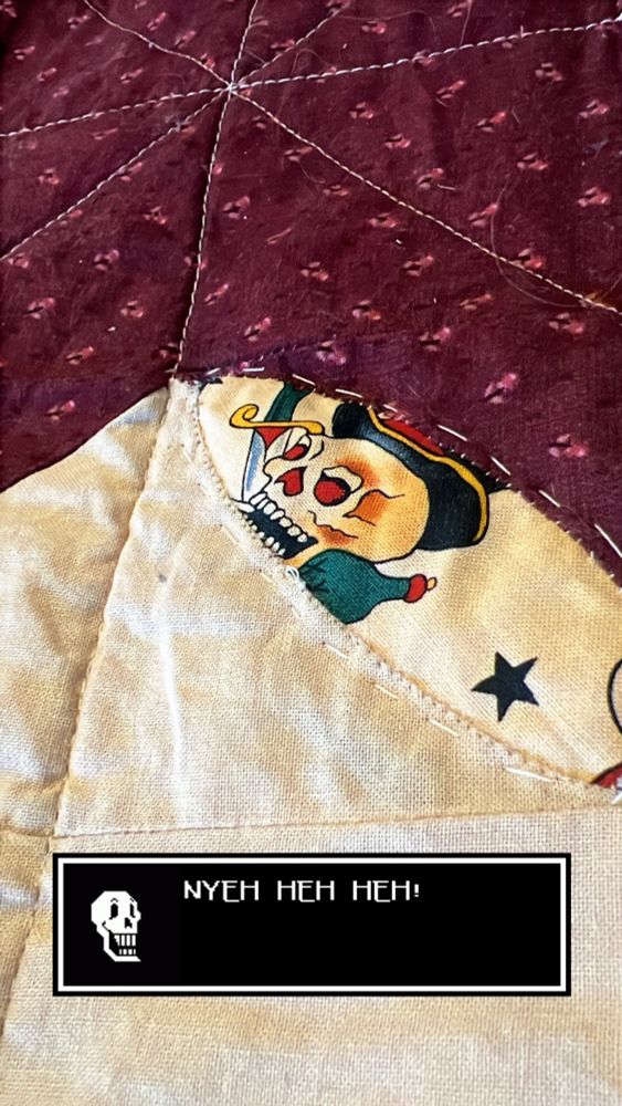 Where a town seam was between the burgundy and tan blocks, now a tan piece of fabric with a skeleton tattoo on it peeks out from behind the tear. The tear has been rolled back and sewn down to make an orange peel shape. The Instagram story caption in this is a black text box from the video game Undertale with Paparyus, a skeleton character, saying “NYEH HEH HEH!”