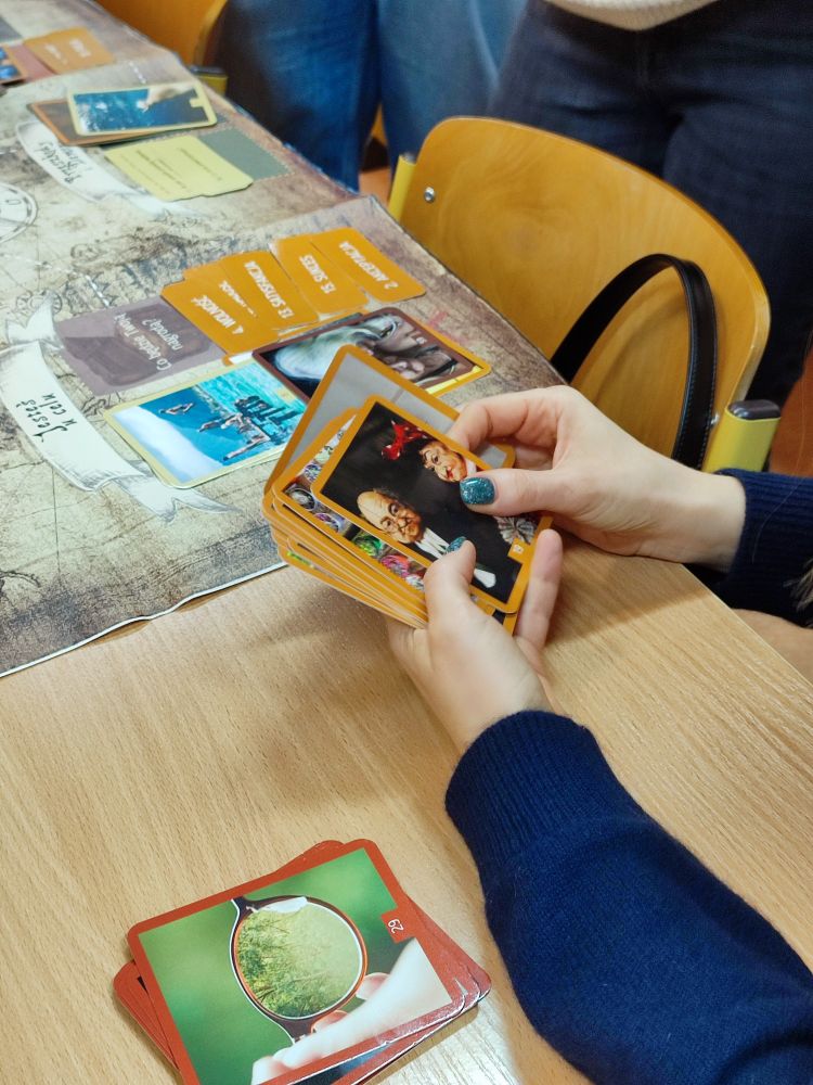 Dłonie trzymające karty, w tle na stoliku widoczne pozostałe karty i plansza.