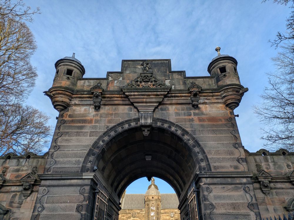 View of the entrance archway (19thc) with turrets etc. The sunlit main building can be glimpsed through the arch.