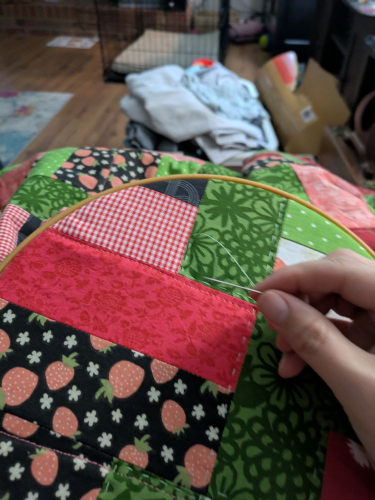 Strawberry patchwork quilt in a hoop, with hand holding a needle to stitch 