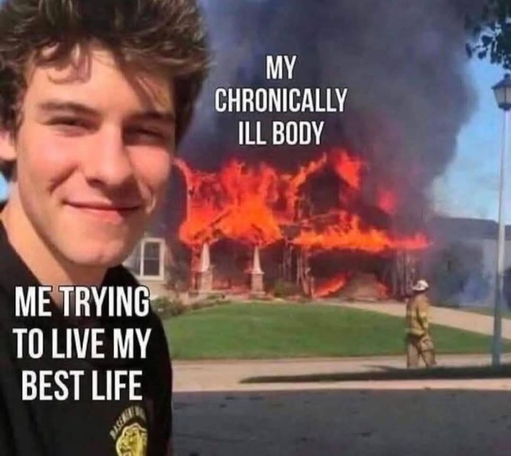 Man looks at camera with a slight grin in the foreground, white text reads "Me trying to live my best life". In the background a house is on fire, white text above it reads "my critically ill body", and a fireman is walking past the house in full gear.