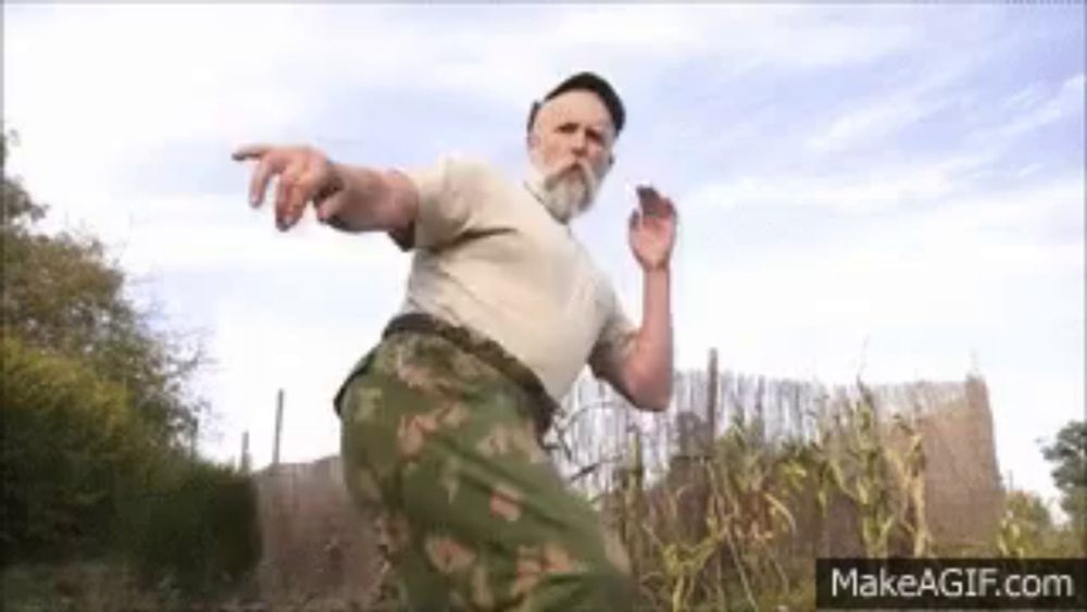 a man with a beard is standing in a field and pointing at something .