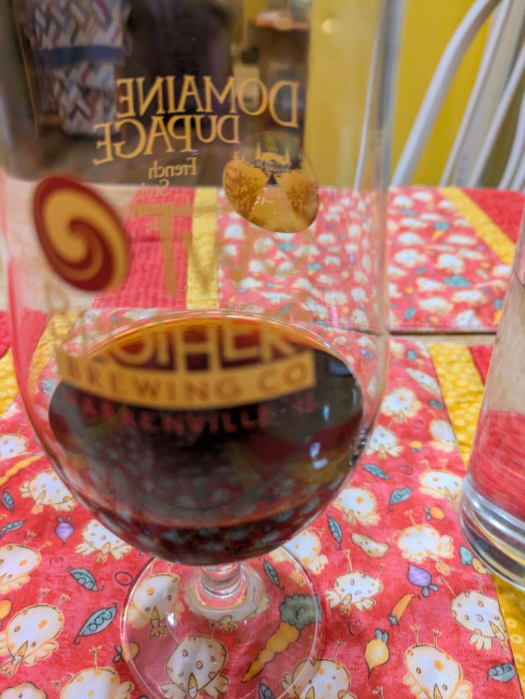 A dark beer out of focus with Domaine Dupage on the glass in focus
