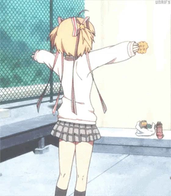 a girl in a skirt is holding a cookie with her arms outstretched in front of a fence .