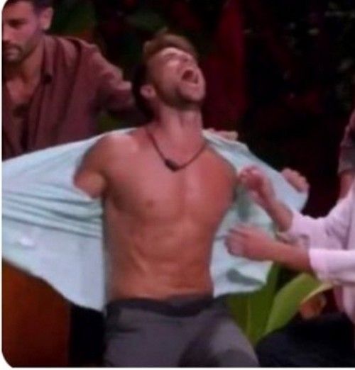 Foto de um homem branco padrão gritando enquanto abre a camisa, mostrando um belíssimo peitoral e uma barriga tanquinho