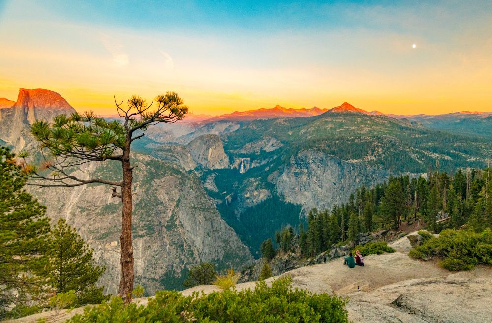Two people sit at watch sunset from Glacier Point in Yosemite
