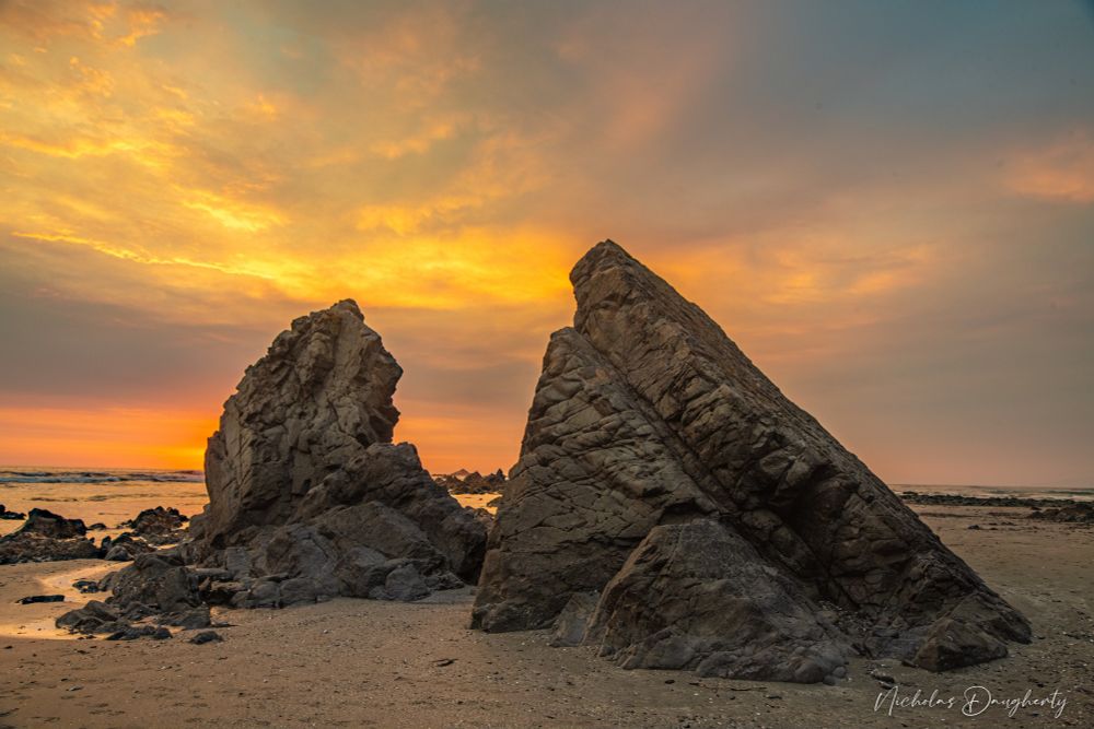 Large rocks on the beach with a bright sunset behind