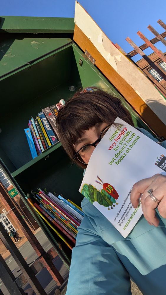 An adult stands in front of a book box at a school. 