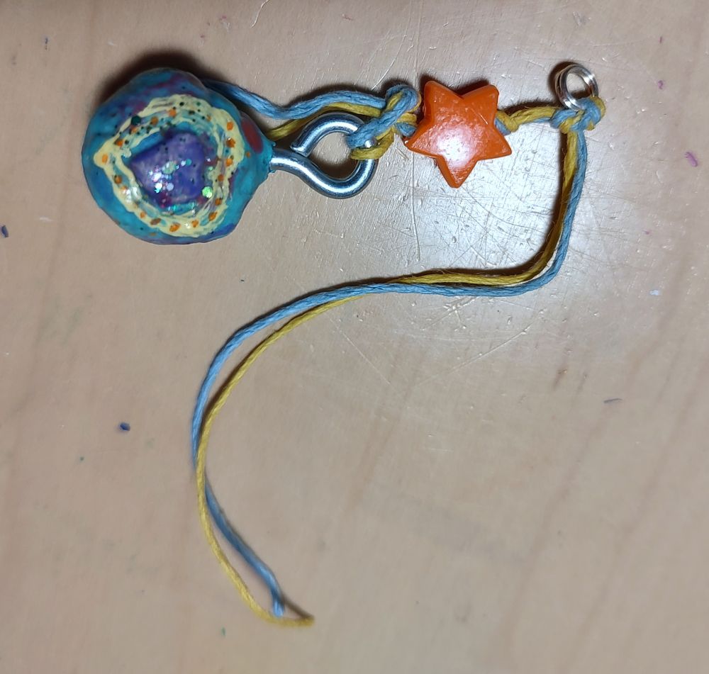 blue sphere with yellow outlined purple sparkling heart ornament with an orange star bead and a blue and yellow string.