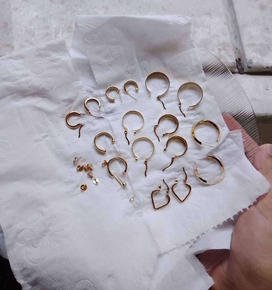 pares de brincos e argolas douradas sob um prato forrado com papel higiênico