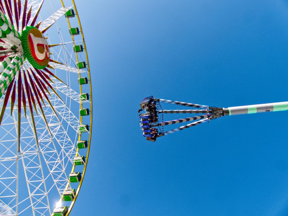 Zwei Fahrgeschäfte bin unten nach oben fotografiert. Riesenrad und eine große Schaukel
