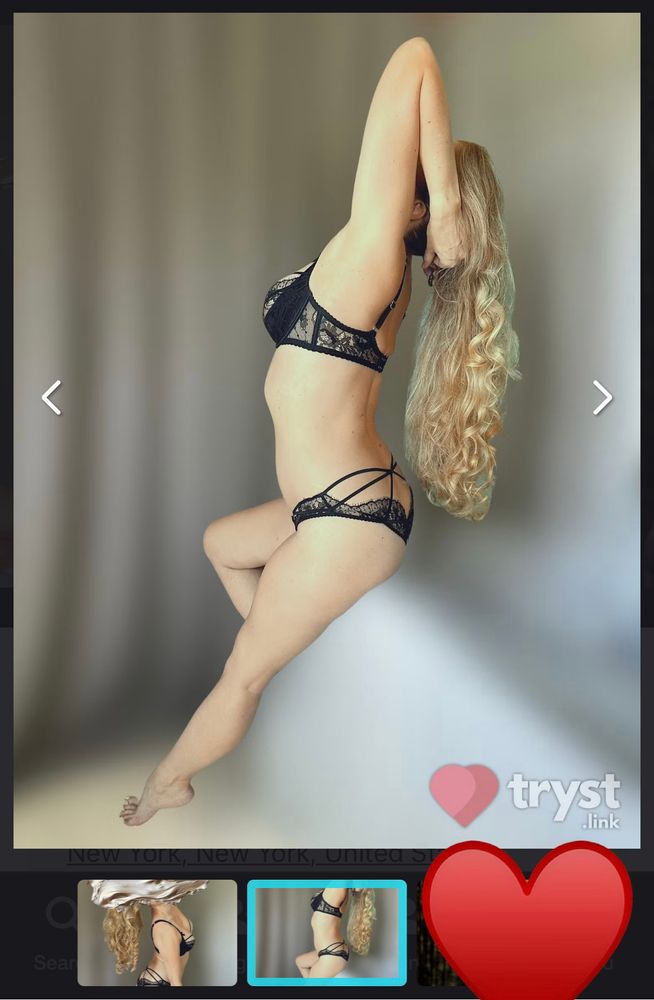 A screenshot from Tryst showing a photo with a grayish blurred background behind Catelyn posing in black lingerie. 