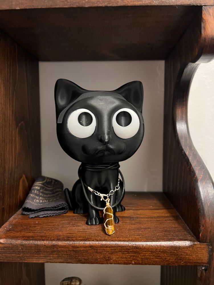 A 3-D printed black cat with giant eyes. He is NOT wearing a pair of folded human glasses.