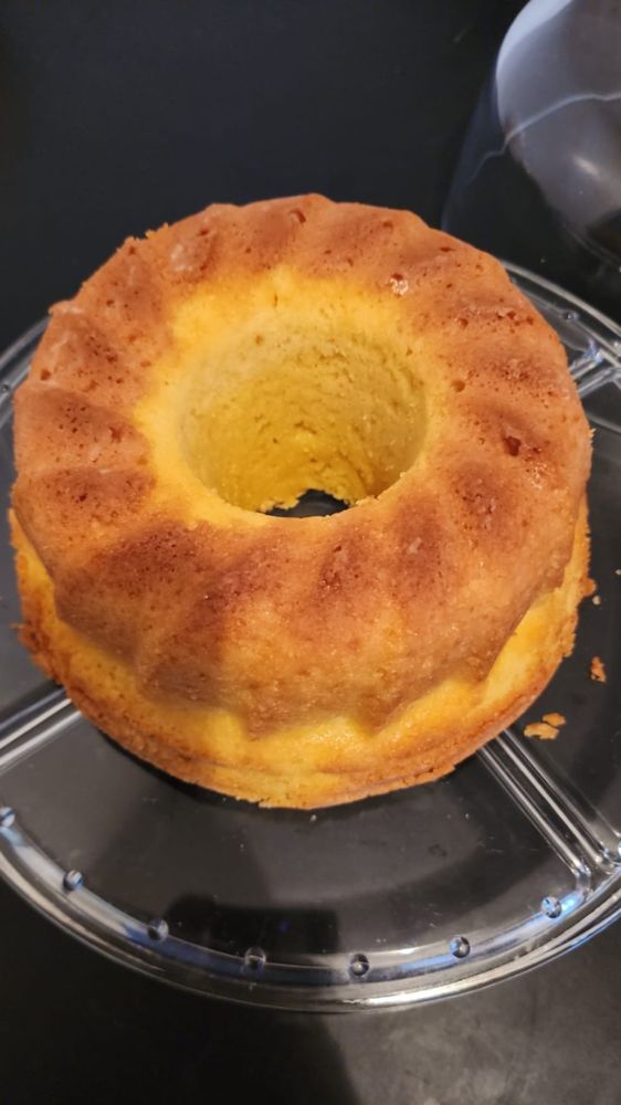 Bolo de fubá recém desenformado, sobre uma boleira de vidro. Ele tem aparência macia.