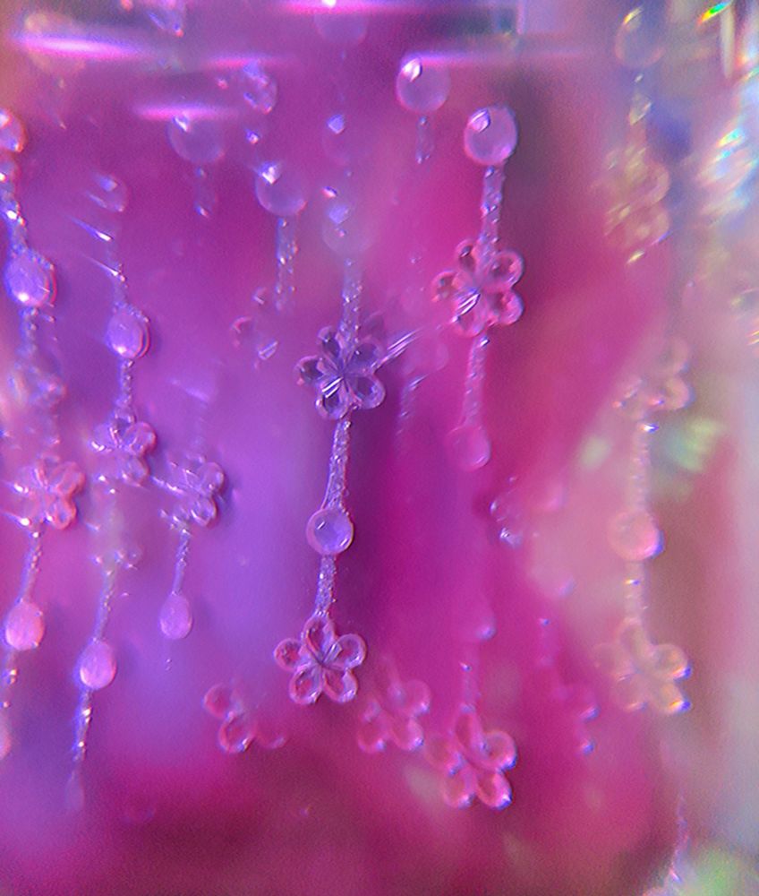 Close up photo of a small pink vase with flowers shaped gems decorations. Added a crystal suncatcher in front of the phone camera to make some kind of aesthetic effect.