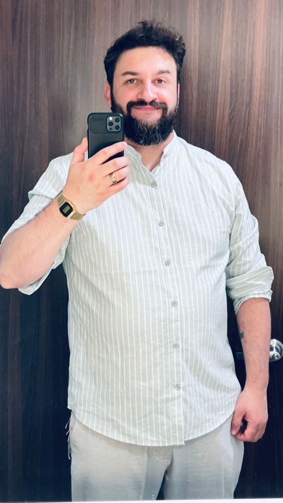 A sexy man wearing a mint green pinstripe shirt and linen pants taking a mirror selfie