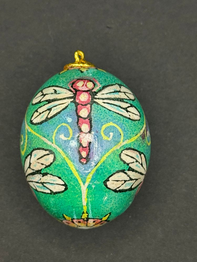 A pysanky style dyed egg with a pattern of pink dragonflies on green and blue background. 