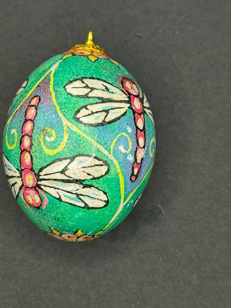 A pysanky style dyed egg with a pattern of pink dragonflies on green and blue background. 