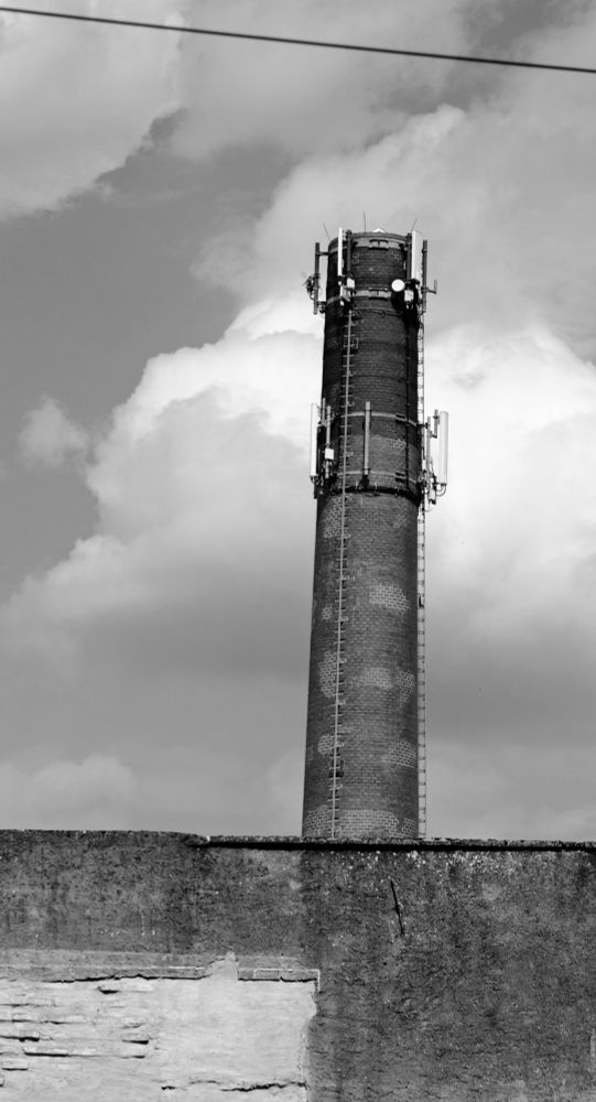 S/W Aufnahme

Alte Mauer, bei der unten links die Steinkonstruktion unter dem Verputz zu sehen ist. Dahinter ein gemauerter, runder Turm mit Drahtlonstruktionen am oberen Ende. Darüber verläuft quer durchs Bild ein dickes Kabel.