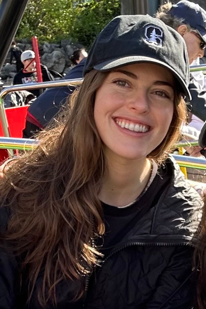Monica wearing black jacket and black baseball cap with Stanford logo (and if you look closely into the background you can see this is cropped from a shot at an amusement park 😅)