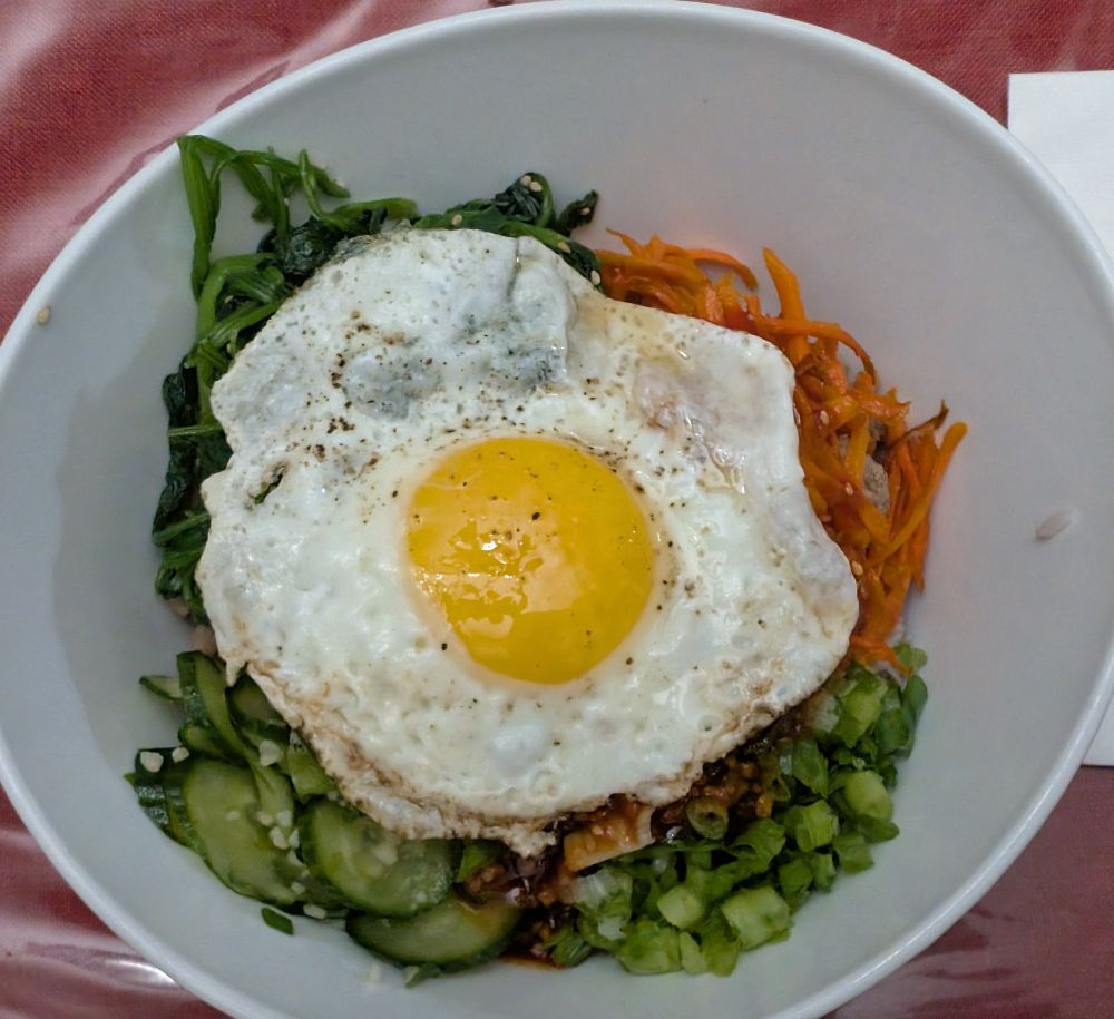 A bowl of bibimbap with a sunny side up egg on top
