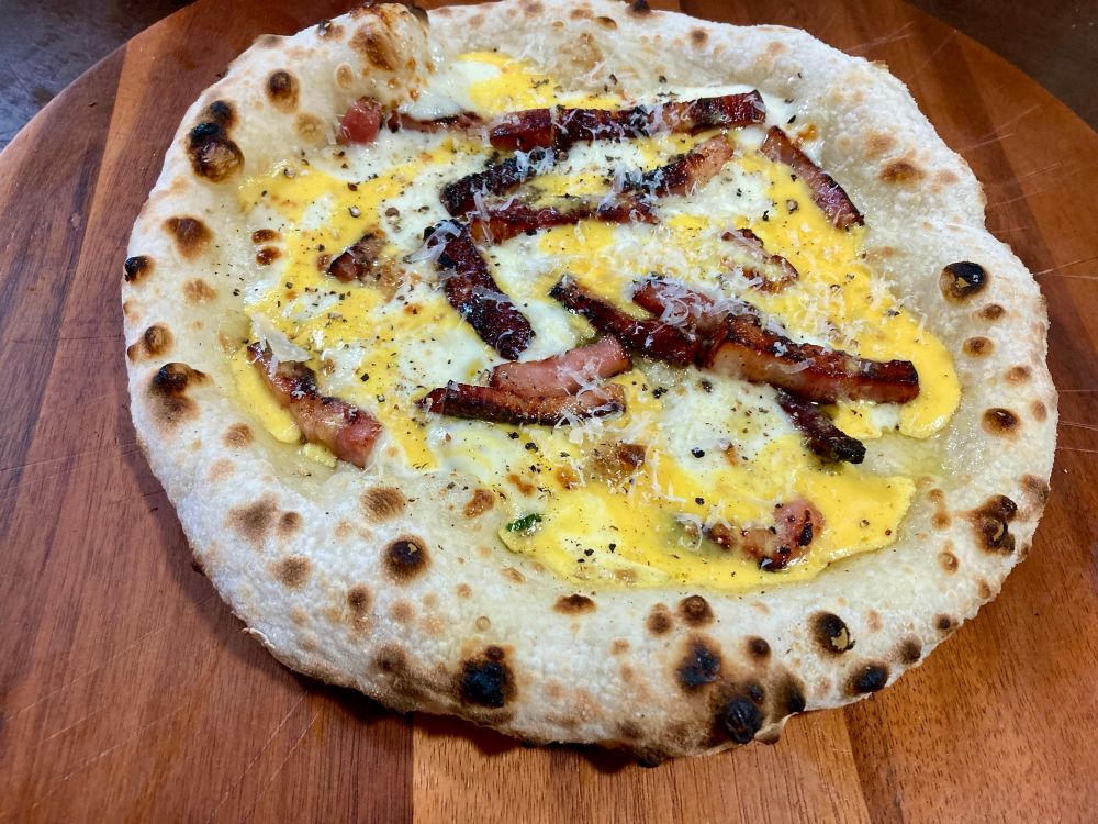 Neapolitan-style pizza topped with mozzarella and bacon for the bake, then drizzled with the traditional carbonara mix of egg yolk, cream, Parmesan and black pepper post-bake. Then more parm and pepper to finish