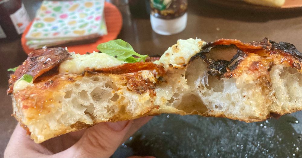 A side view of a mammoth slice of airy pizza. About an inch and a half thick! 