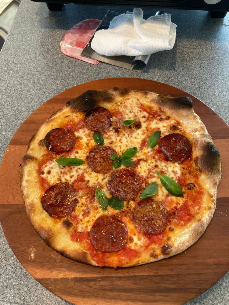 Thin and crispy Roman pizza aka scrocchiarella on a wooden board, with mozzarella and chorizo. Topped with basil and Parmesan 