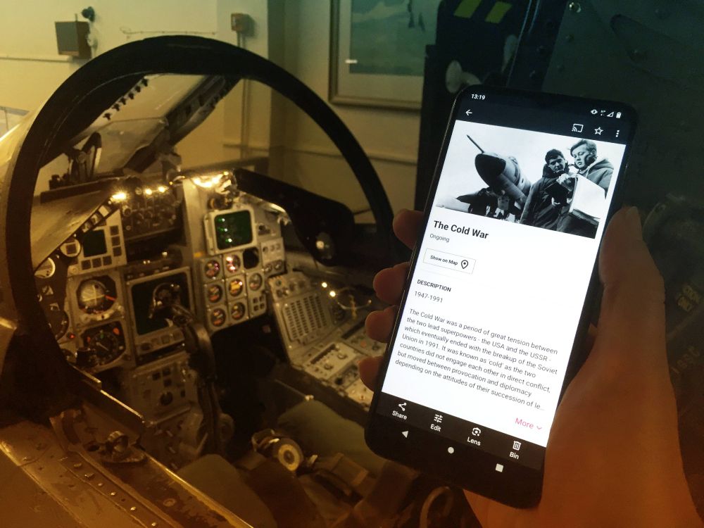 photo, colour, a person holding a phone with the Bloomberg Connects digital guide to the RAF Air Defence Radar Museum. In the background is the cockpit of a Tornado F3. 