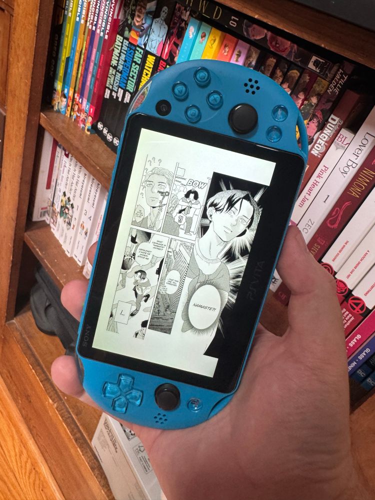 Love in the Palm of his hand being read on a ps vita with a shelf of Manga and comics in the background 