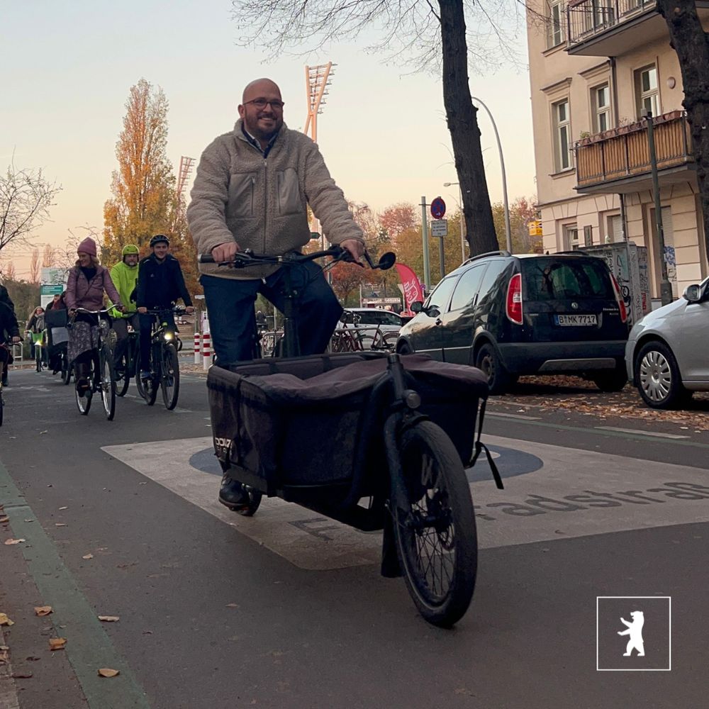 Zu sehen ist Bezirksstadtrat Christopher Schriner, der mit einem Lastenrad auf einer Fahrradstraße fährt. Im Hintergrund sind weitere Fahrradfahrer*innen.