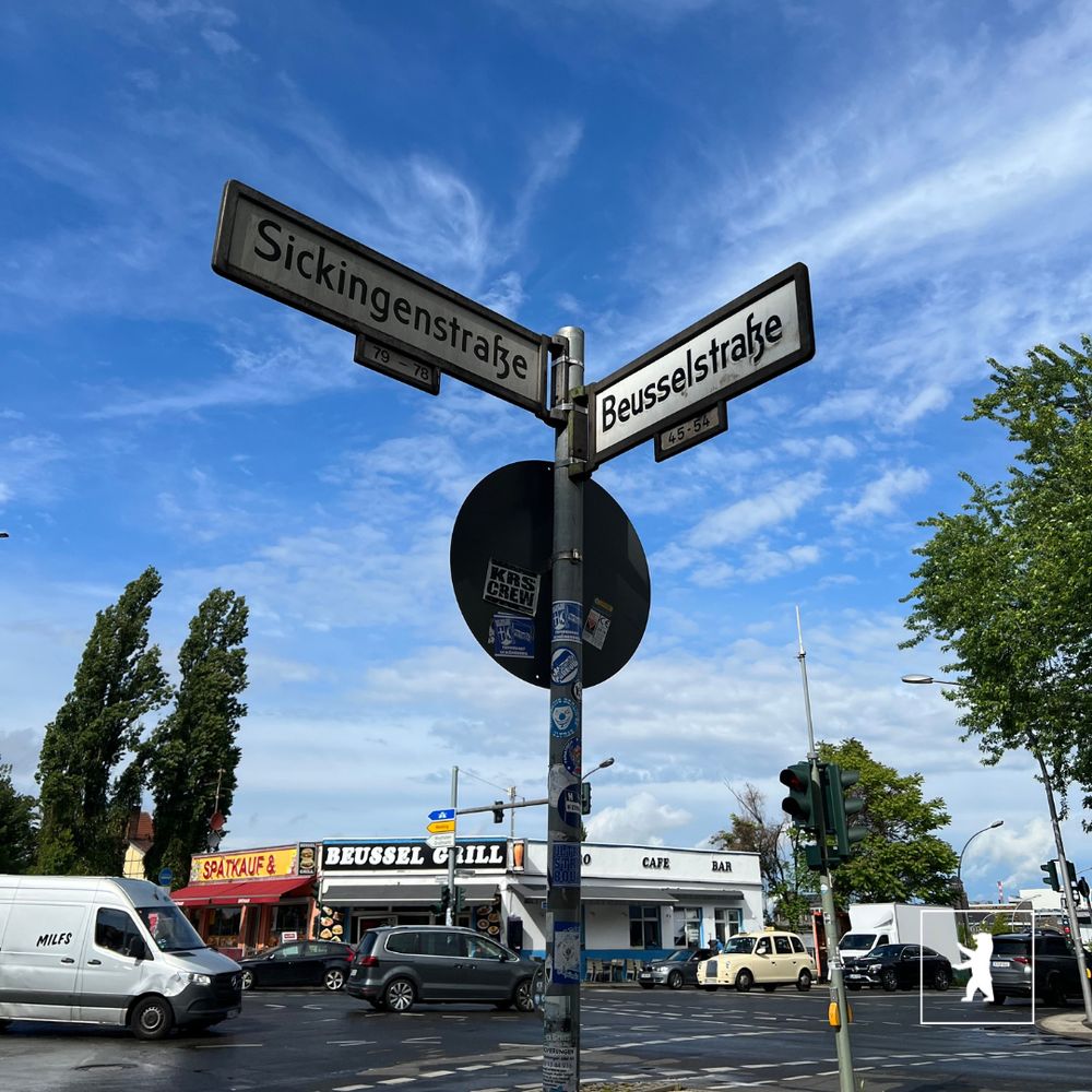 Die Kreuzung Sickingenstraße Ecke Beusselstraße. Der Himmel ist blau nachdem die Regenwolken vorbei gezogen sind. die Straße ist noch nass. Autos fahren auf der Straße. Im Hintergrund ist ein Imbiss zu sehen.