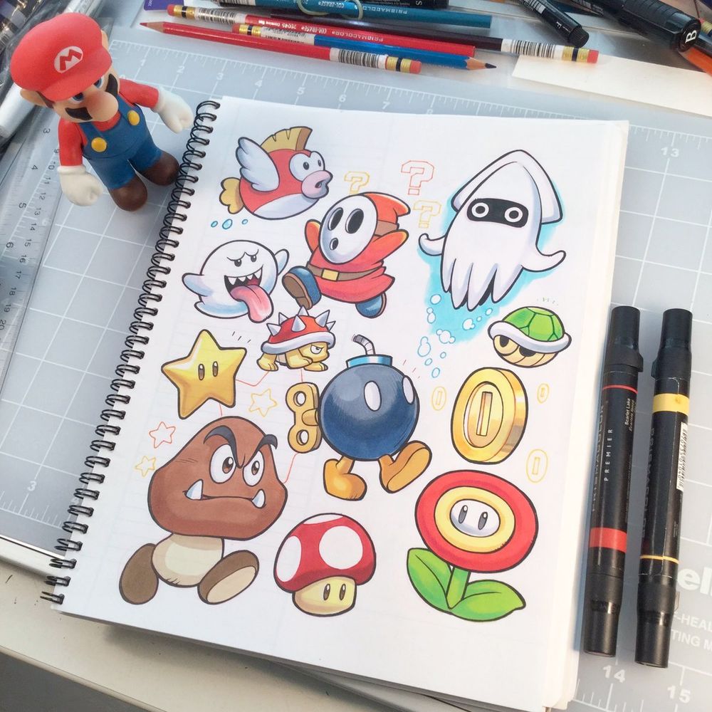A sketchbook page with a variety of Mario items and enemies drawn in pen and ink and marker.  There's a toy Mario standing near the top left corner and two Prismacolor markers on the right.