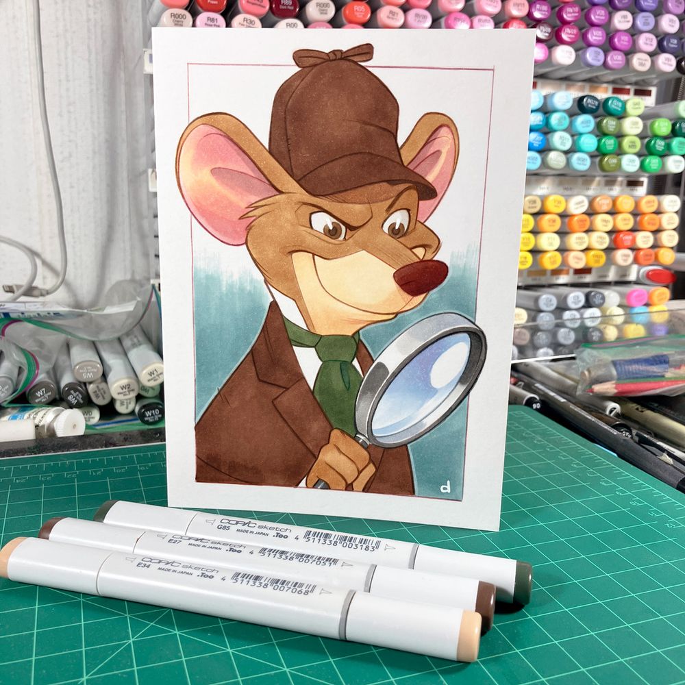 A custom birthday card with a drawing of The Great Mouse Detective. Three Copic markers are sitting on the desk in front of it and you can see a rack full of markers in the background along with a clutter of other art supplies.